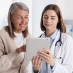 Smiling healthcare worker and senior patient looking at a tablet.