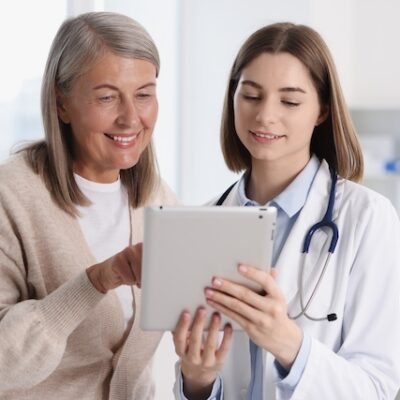 Smiling healthcare worker and senior patient looking at a tablet.